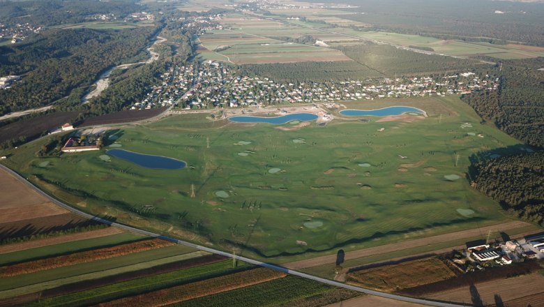 Luftaufnahme eines Golfplatzes mit mehreren Wasserhindernissen und angrenzender Siedlung.