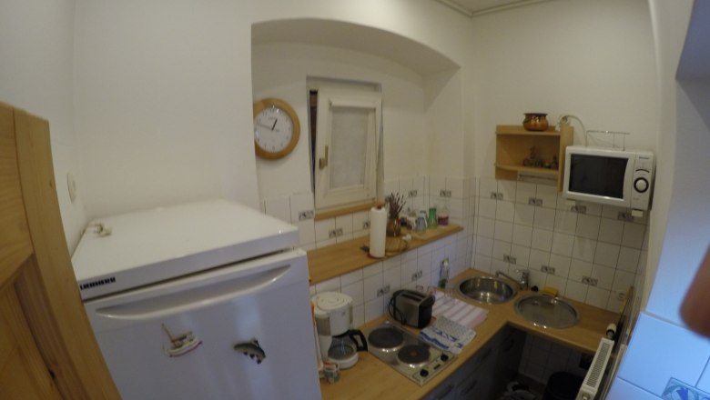 Kleine Küche mit Kühlschrank, Mikrowelle, Herd und Spüle.