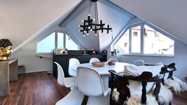 Moderner Essbereich in einem Dachgeschoss mit weißen Stühlen, Holzboden und einem großen Fenster.