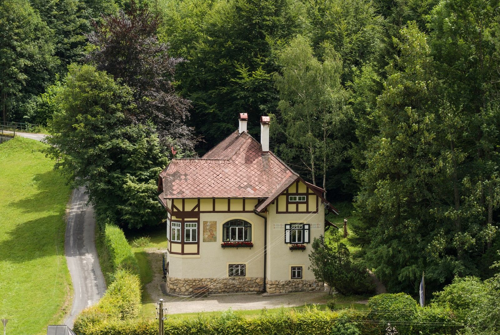 A two-storey house in traditional style, surrounded by dense forest and a well-tended garden.