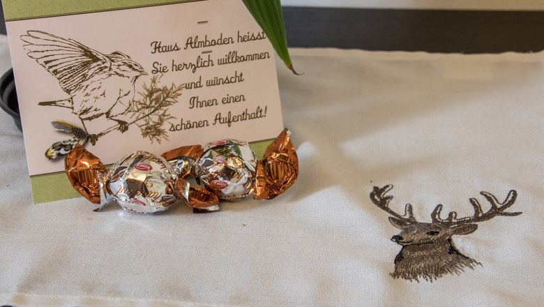 Welcome card with bird drawing and chocolates on a tablecloth with deer motif.