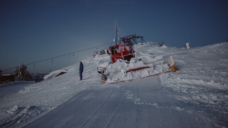Eine Pistenraupe auf einer verschneiten Skipiste bei Dämmerung im Schigebiet Unterberg.