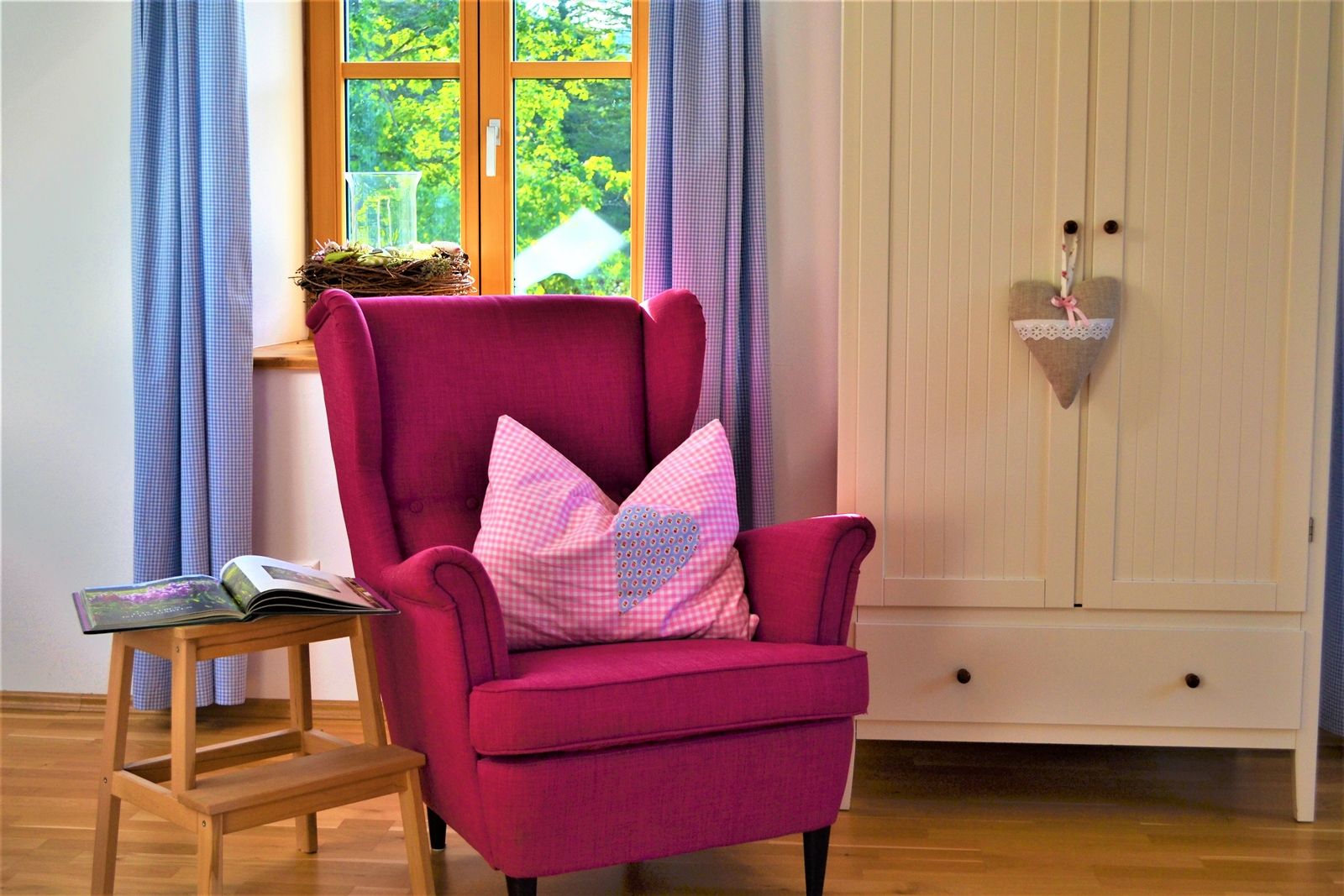 Gemütliches Zimmer mit pinkem Sessel, Kissen, kleinem Tisch und Schrank.