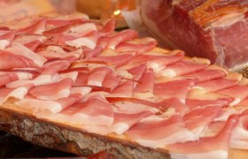 Nahaufnahme von dünn geschnittenem Speck auf einem Holzbrett.