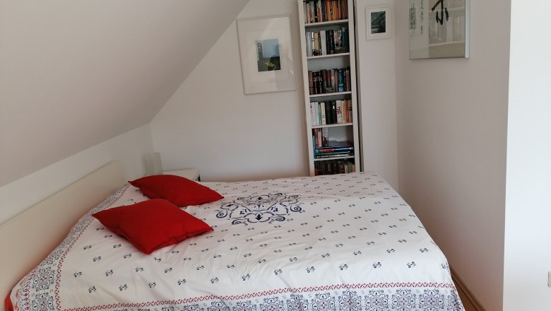 Schlafzimmer mit Bett, roten Kissen und B&uuml;cherregal.