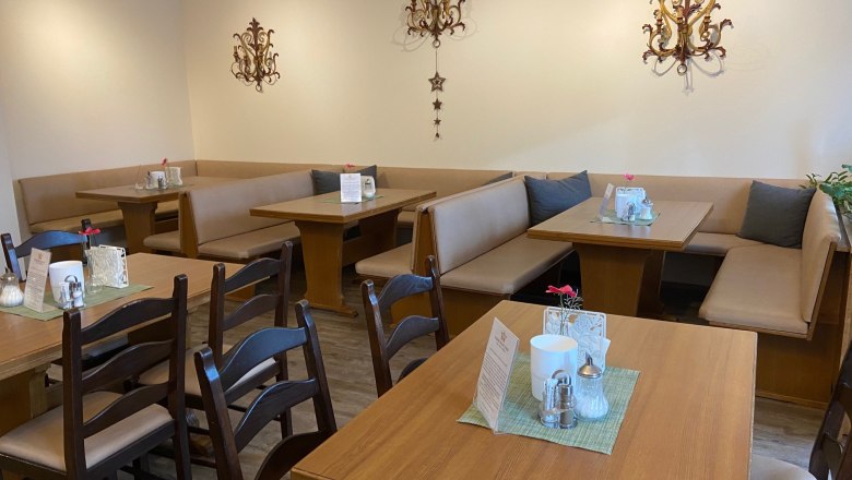 Gemütlicher Frühstücksbereich mit Holztischen und gepolsterten Sitzbänken, dekoriert mit Wandornamenten.