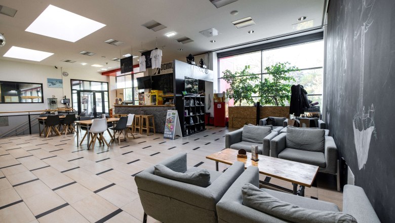 Innenansicht eines Cafés mit grauen Sofas, Holztischen und einer Bar im Hintergrund.