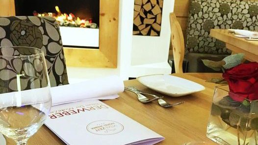 Innenansicht eines Restaurants mit Tischgedeck, Weinglas, Menü und Kamin.