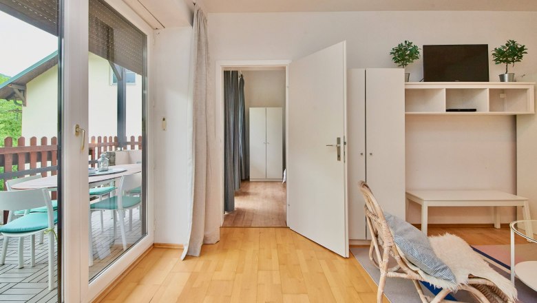 Bright living room with wooden floor, glass door to the terrace, white furniture and plants.