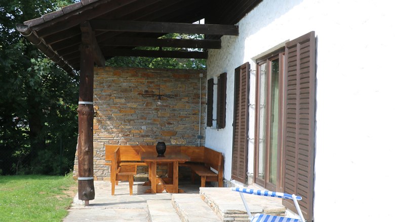 Terrasse mit Liege und Holzmöbeln neben einem Haus mit Schindeldach.