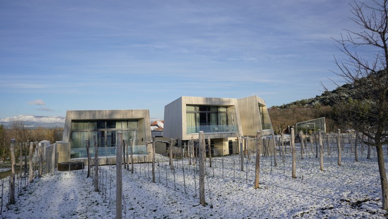 Modern garden lofts covered in snow in winter, surrounded by bare trees and a clear blue sky.