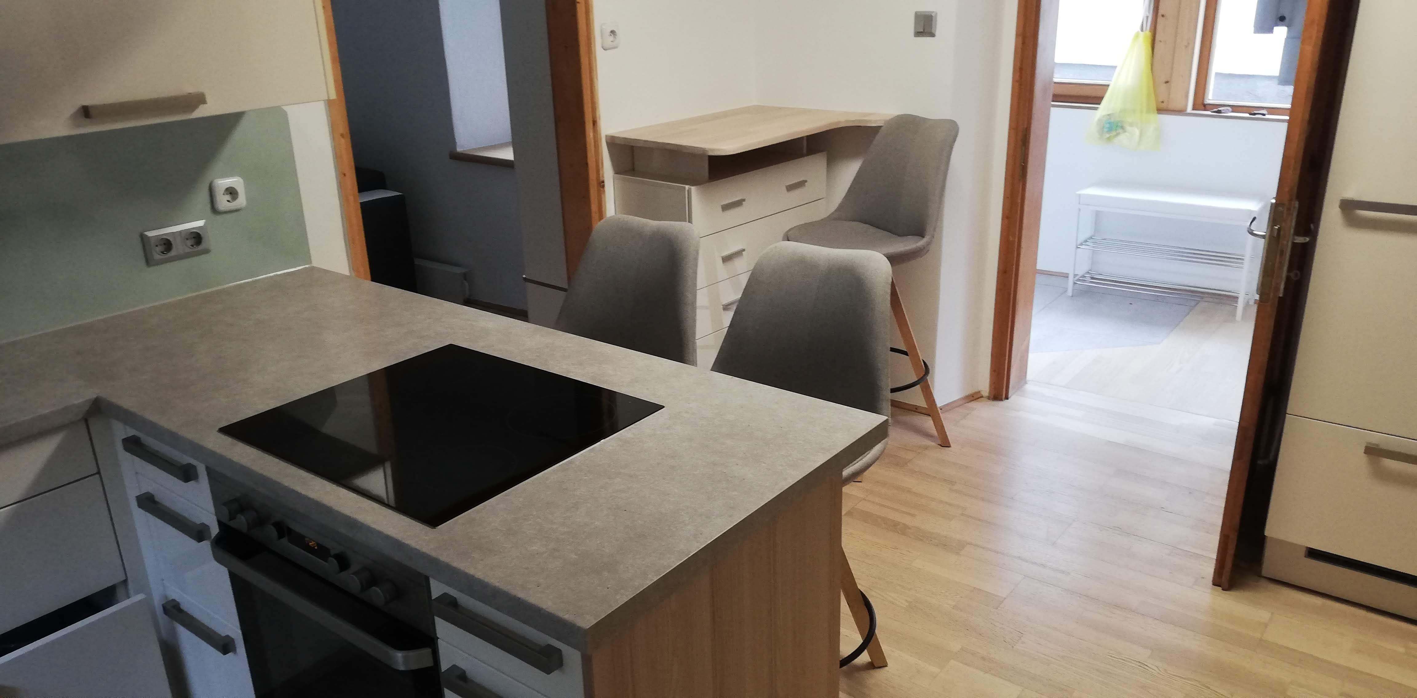 Moderne Küche mit Kochinsel, zwei grauen Stühlen und Holzfußboden.