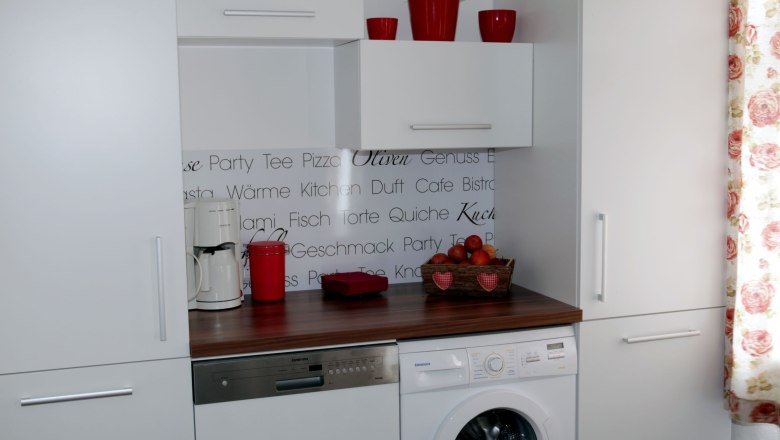 Küchenzeile mit Waschmaschine, Geschirrspüler, Kaffeemaschine und Dekoration.