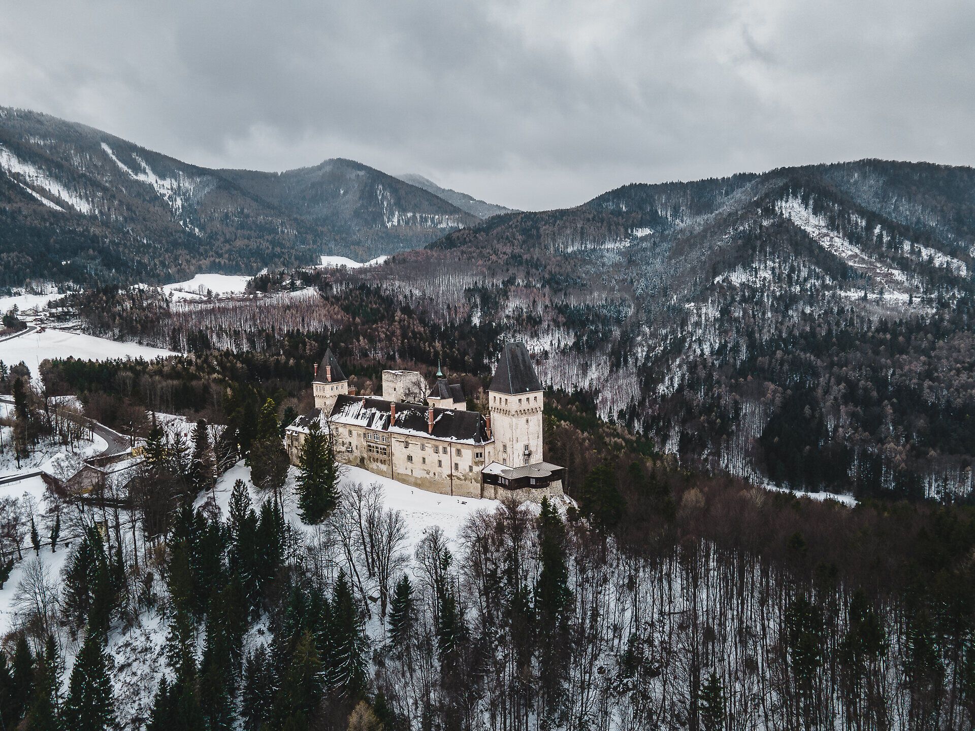 Inmitten einer winterlichen Märchenlandschaft erhebt sich majestätisch ein historisches Schloss, umgeben von schneebedeckten Bergen und dichten Wäldern. Die kalte Luft ist frisch und klar, während die sanften Hügel in der Ferne eine ruhige, friedliche Atmosphäre schaffen. Ein perfekter Ort für Naturliebhaber und Geschichtsinteressierte, die die Schönheit der Alpen im Winter erleben möchten.