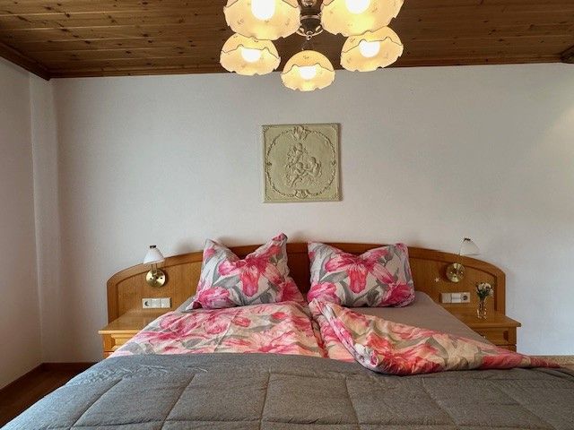 Ein gemütliches Schlafzimmer mit einem Doppelbett, floralem Bettzeug und einer Holzdecke. Eine Lampe hängt von der Decke.