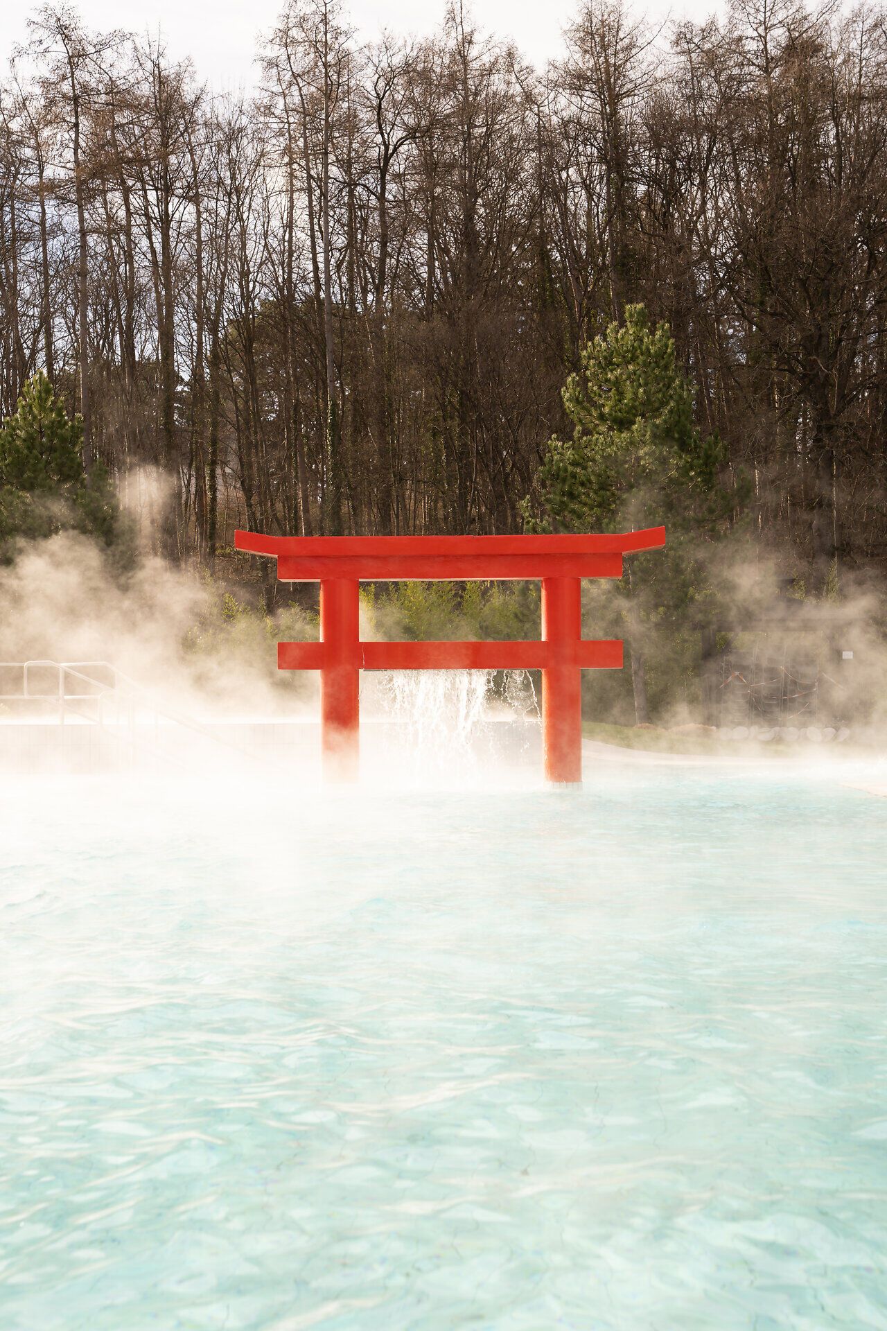 Inmitten dampfender Quellen erhebt sich ein leuchtend rotes Tor, das an die fernöstliche Kultur erinnert. Umgeben von einer malerischen Landschaft, lädt dieser Ort zur Entspannung und Erholung ein. Die sanften Wellen des Wassers reflektieren die Schönheit der Natur und schaffen eine harmonische Atmosphäre.