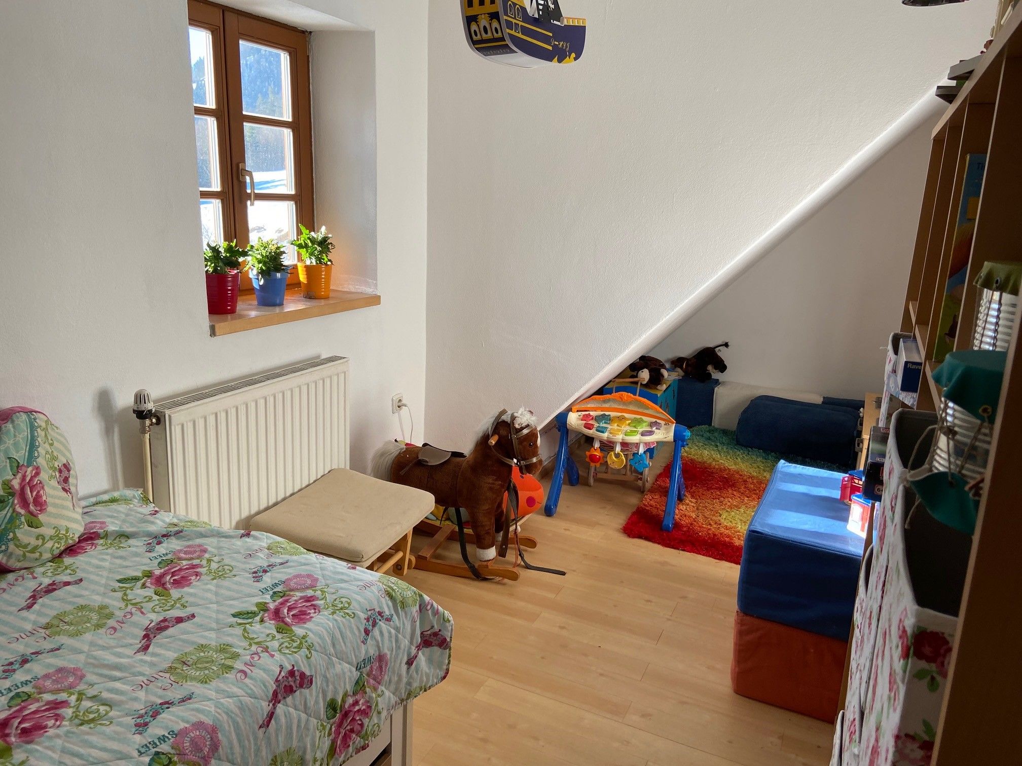 Kinderzimmer mit Bett, Spielzeug und buntem Teppich.