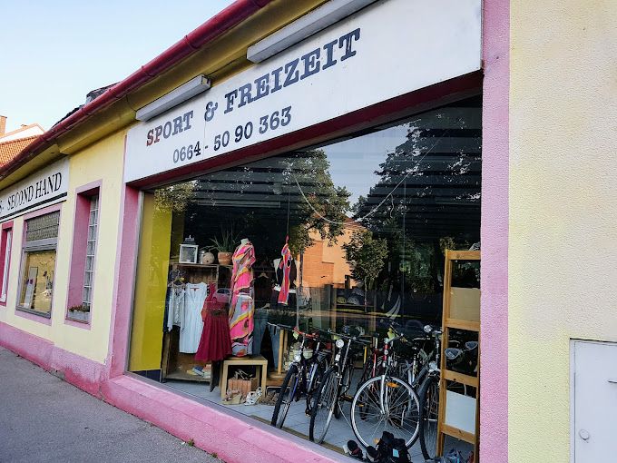 Schaufenster eines Second-Hand-Ladens mit Kleidung und Fahrrädern.