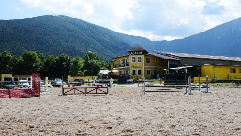 Halmerhof riding stables with jumping arena and mountains in the background.
