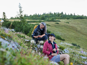 Inmitten der atemberaubenden Landschaft der Raxalpe genießen zwei Wanderer eine wohlverdiente Pause. Umgeben von blühenden Alpenkräutern und sanften Hügeln strahlt die Szenerie eine friedliche Atmosphäre aus, die zum Verweilen einlädt.