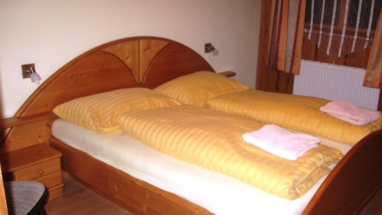 Holzbett mit gelber Bettwäsche in einem Zimmer.