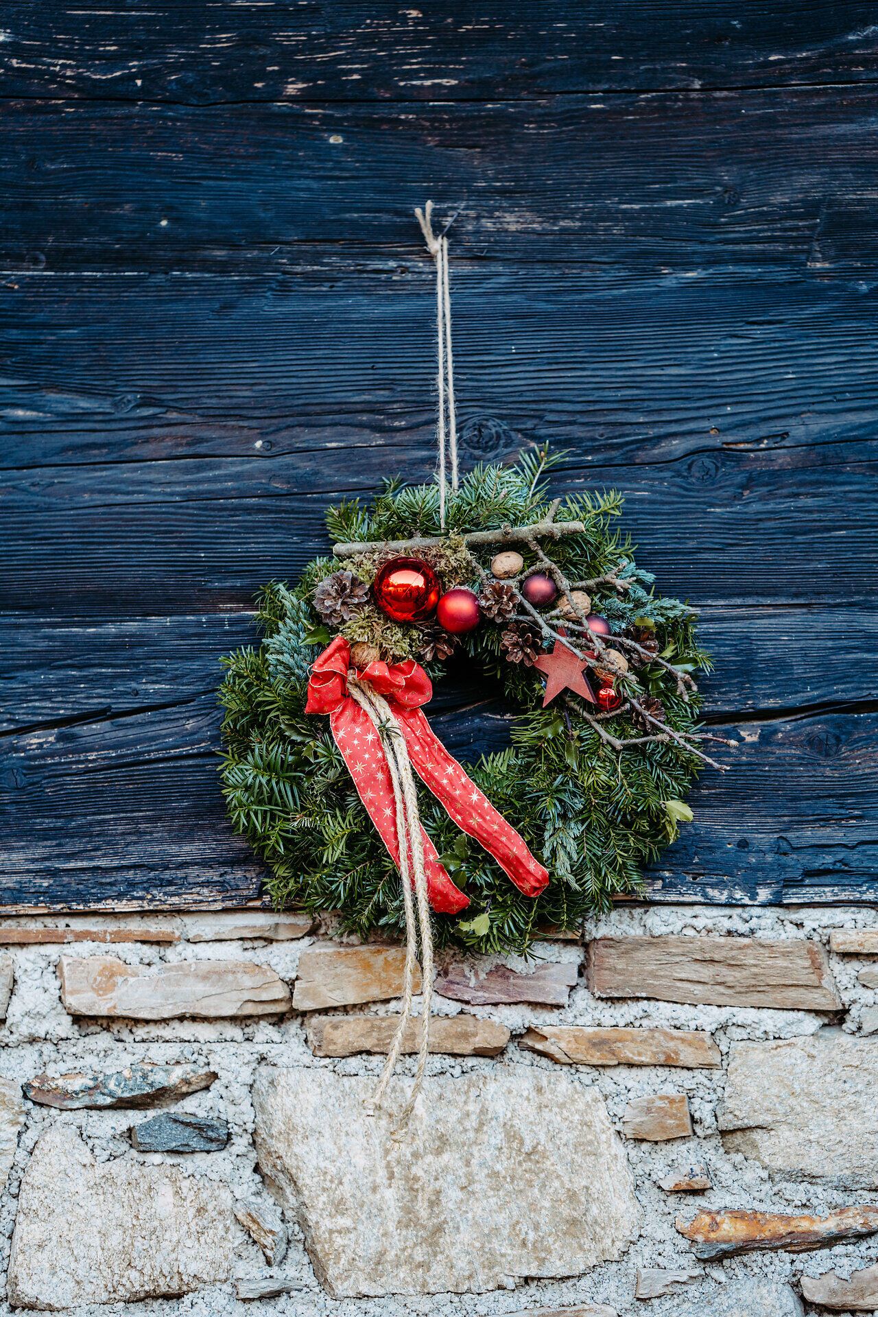 Grüner Adventskranz mit roten Schleifen an einer dunklen Holzwand.