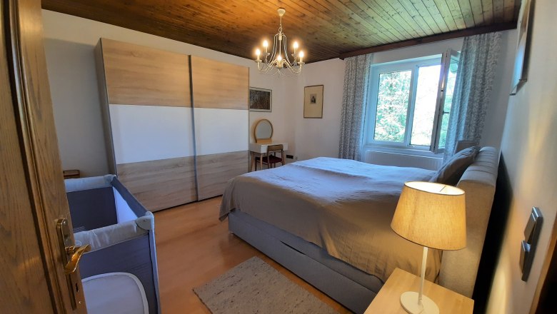 Ein gemütliches Schlafzimmer mit Holzboden, Doppelbett, Kleiderschrank, Kinderbett und Nachttischlampe.