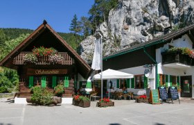 Ein traditionelles Gasthaus mit Holzbalkon und Blumenschmuck vor einer Felswand.