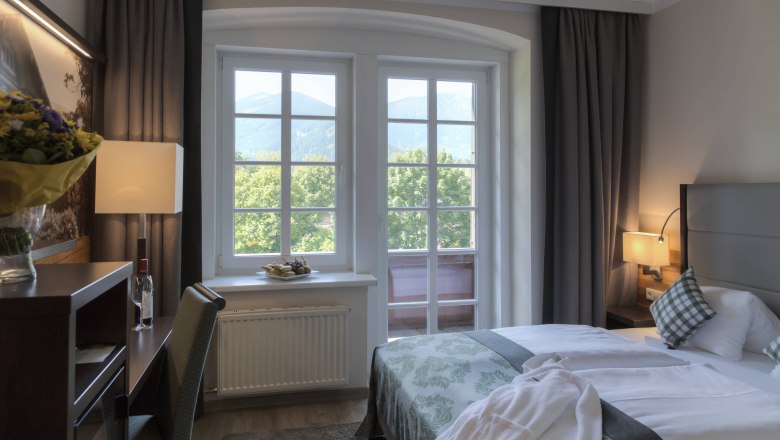 A cozy hotel room with double bed, window with mountain view, desk and flowers.