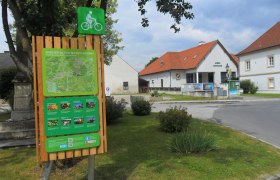 Radstartplatz-Tafel in Walpersbach mit Karte und Informationen, umgeben von Gebäuden und Bäumen.