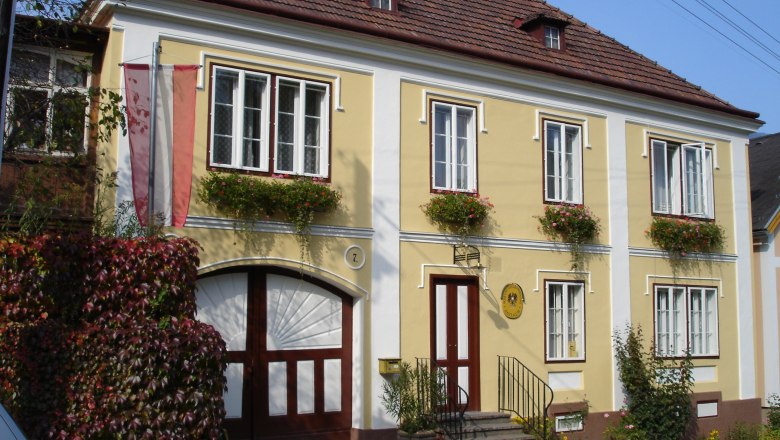 Gelbes Gebäude mit roten Fensterläden und Blumen, nostalgisches Postamt Küb.