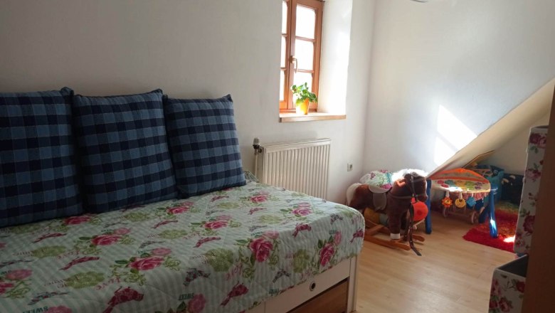 Children's room with pull-out bed, plaid cushions, toy horse and play table. Bright window with plant.