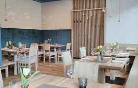 Modern restaurant with wooden furniture, laid tables, ceiling lamps and blue accents.