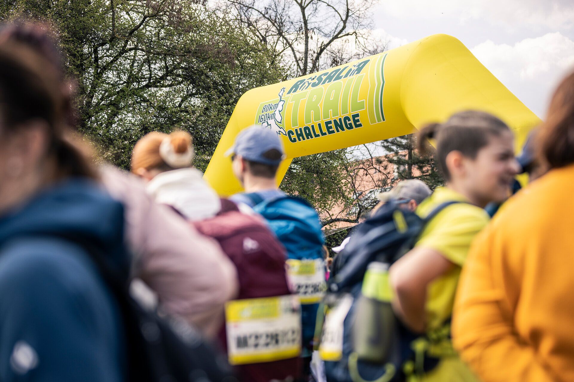 Vor dem Startbogen der „Rosalia Trail Challenge“ stehen einige Teilnehmer mit Startnummern auf ihren Ruchsäcken.
