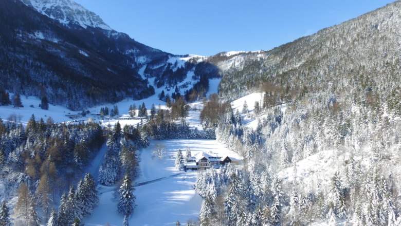 Winterlandschaft mit verschneiten Bergen und einem Hof im Tal.