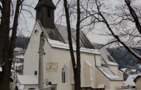 Eine Kirche im Winter mit schneebedecktem Boden und kahlen Bäumen.