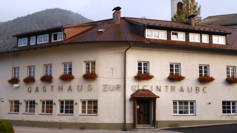 Ein traditionelles Gasthaus mit Blumen an den Fenstern und einem Kirchturm im Hintergrund.