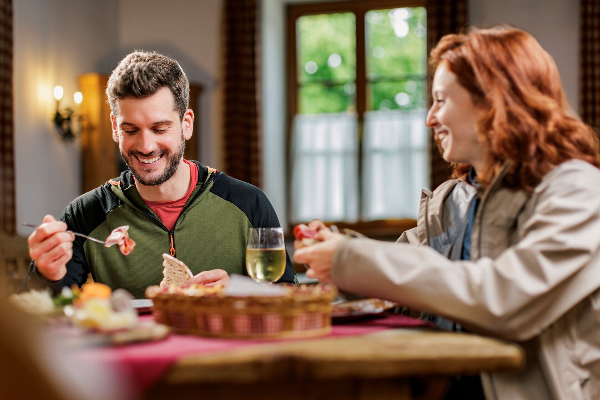 Ein Frau und ein Mann sitzen an einem Tisch und essen eine kalte Heurigenjause mit Wurst und Brot.