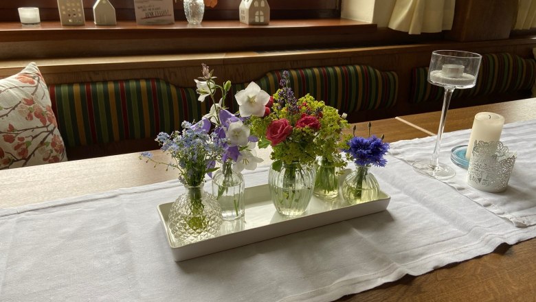 Ein Tisch mit einer weißen Tischdecke, dekoriert mit kleinen Vasen voller bunter Blumen und Kerzenhaltern.