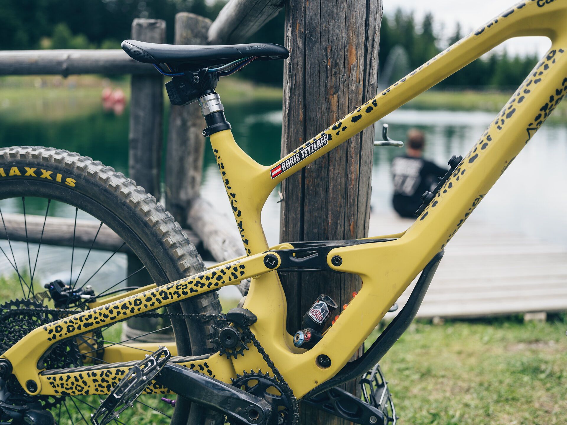 Ein strahlend gelbes Mountainbike mit einem einzigartigen Leopardenmuster steht bereit, um die aufregenden Trails zu erkunden. Im Hintergrund spiegelt sich die ruhige Wasseroberfläche eines Sees, während ein Besucher die friedliche Atmosphäre genießt. Hier in den Wiener Alpen erwartet Abenteurer eine perfekte Kombination aus Natur und Nervenkitzel.