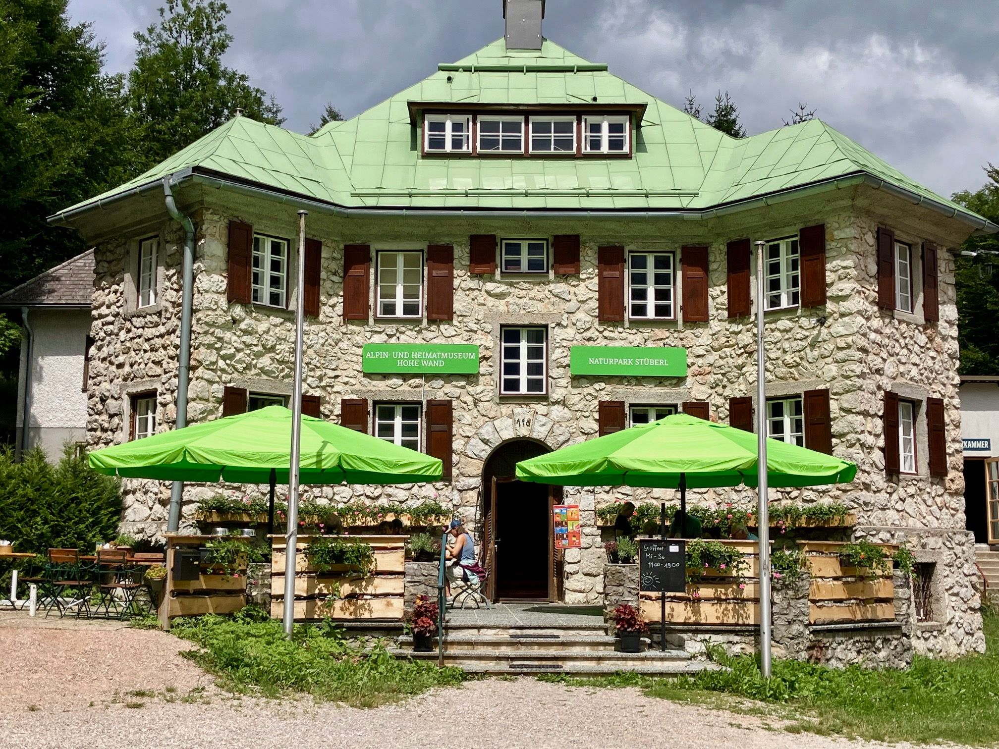 Ein steinernes Gebäude mit grünem Dach und grünen Sonnenschirmen vor dem Eingang, beschriftet mit 'Naturpark Stüberl'.