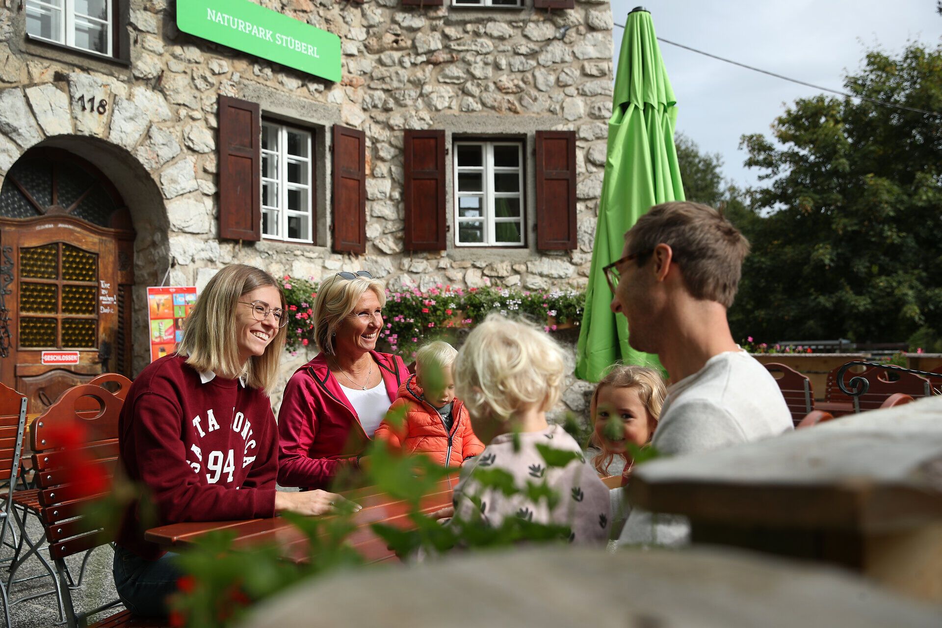 Family and friends are sitting at an outdoor table in front of the Naturpark Stüberl in the Hohe Wand Nature Park.