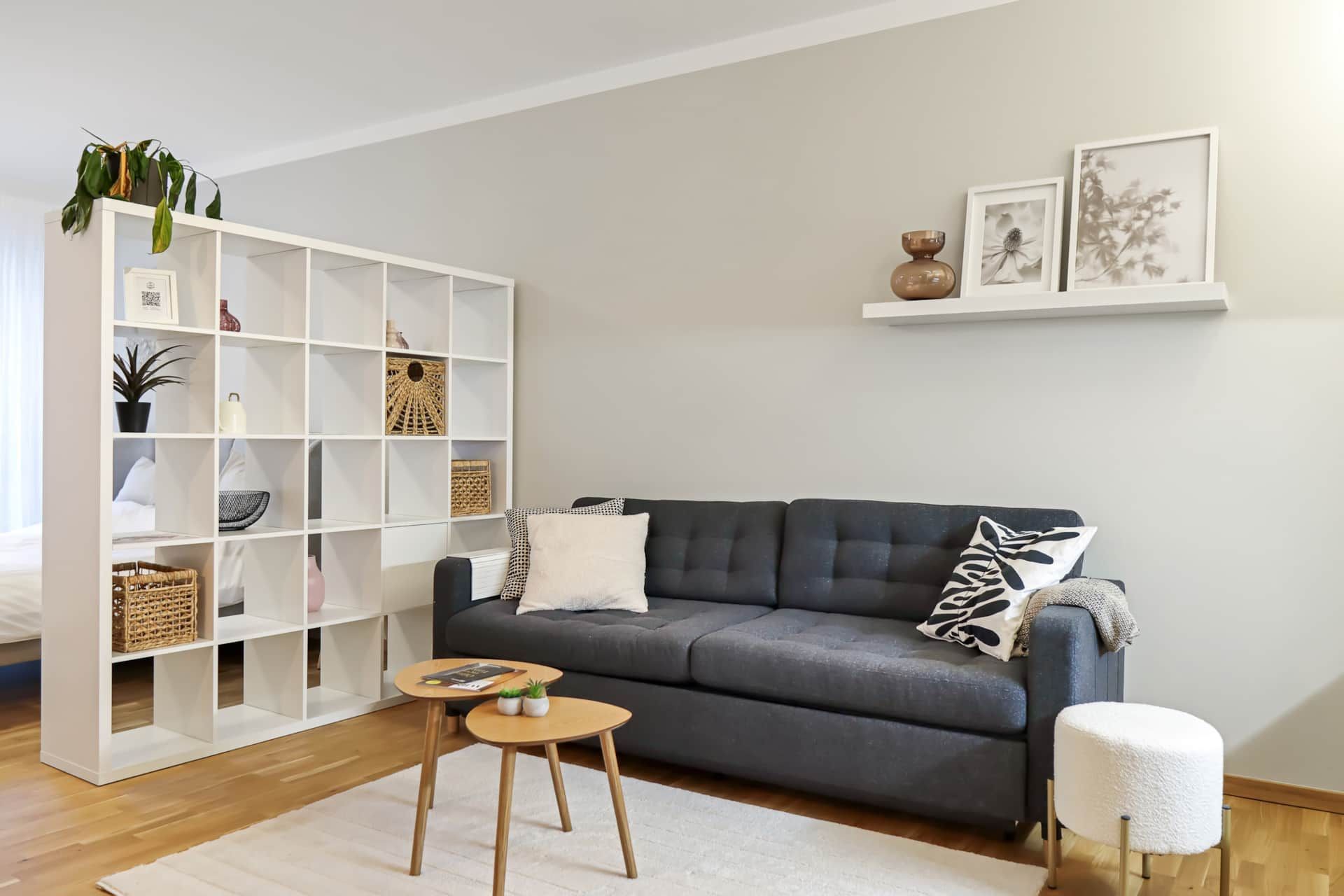 Helles Wohnzimmer mit grauer Couch, Raumteiler und beigen Wänden