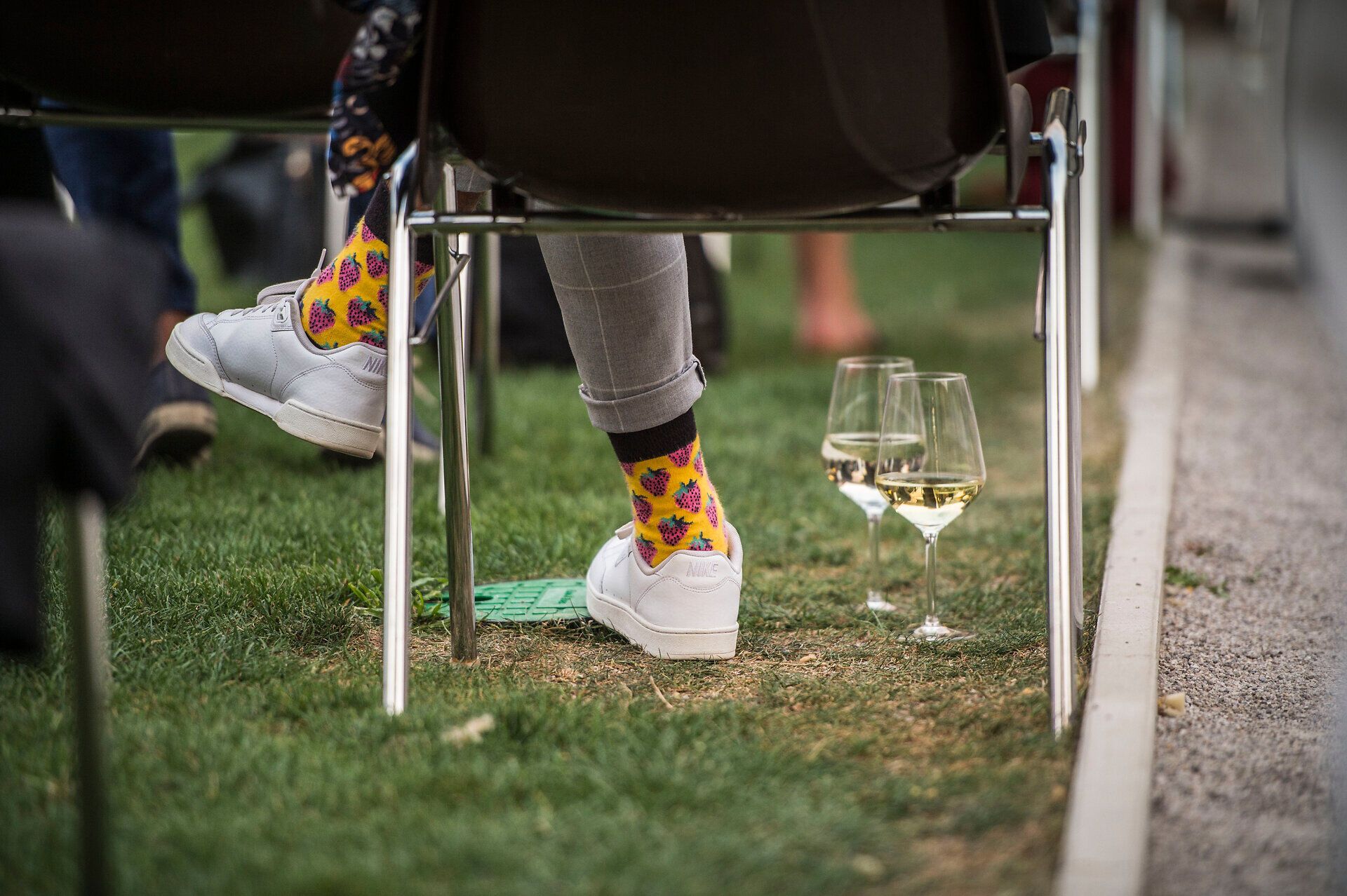 Inmitten der grünen Wiesen und dem sanften Rauschen der Gläser entfaltet sich eine entspannte Atmosphäre. Bunte Socken und weiße Sneakers verleihen dem Moment eine fröhliche Note, während die Gäste den Sommer in vollen Zügen genießen. Ein perfekter Ort, um die Seele baumeln zu lassen und die Schönheit der Natur zu erleben.