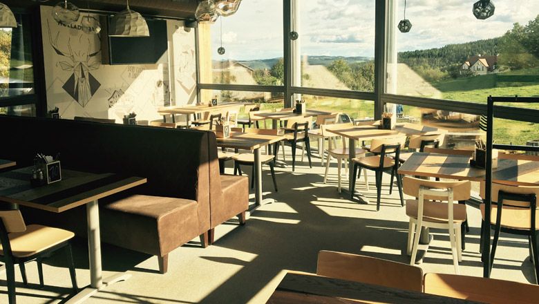 Innenansicht der Wexl Lounge mit Tischen und Stühlen, große Fenster mit Blick auf die Landschaft.