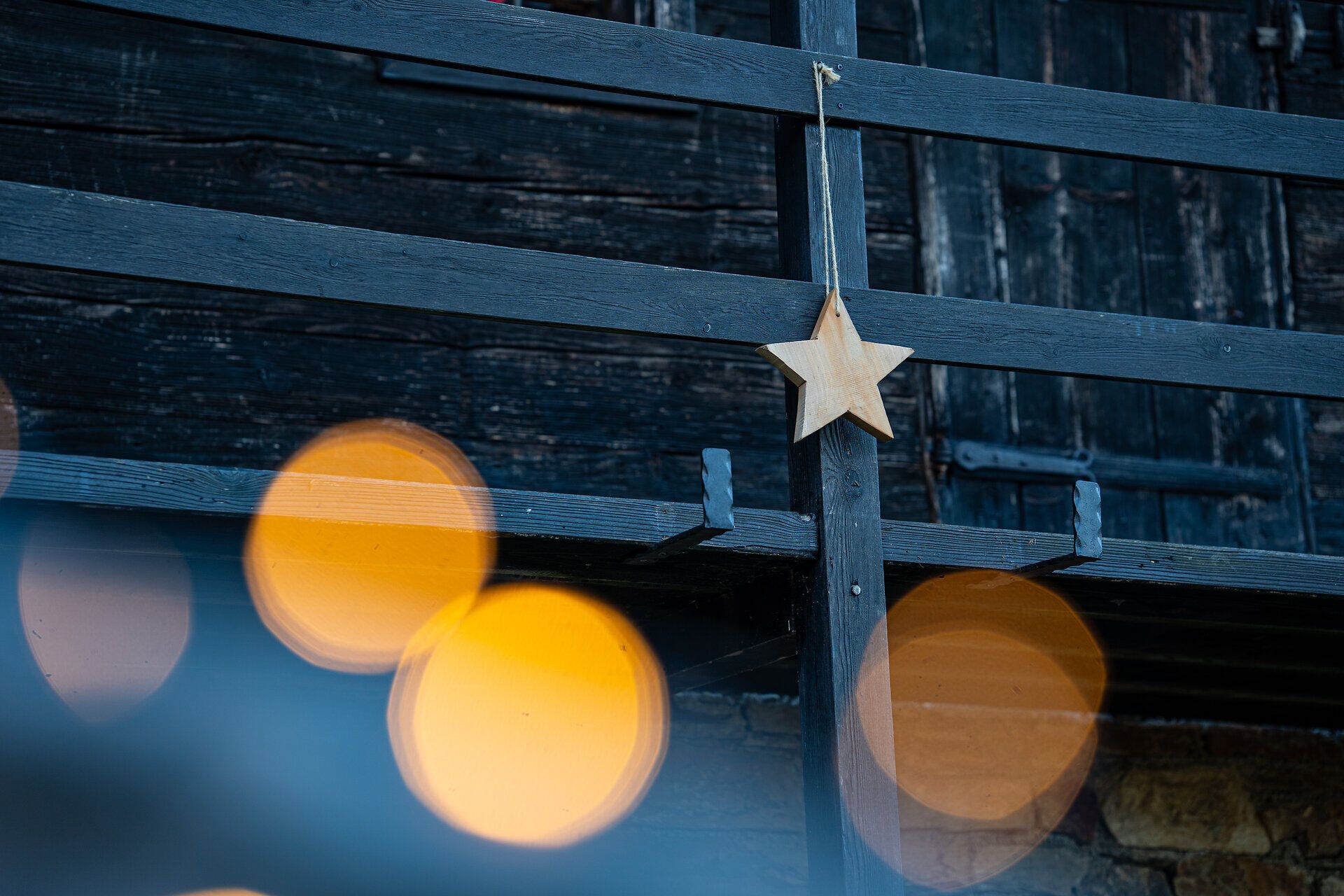 Hängender Holzstern vor dunkler Holzwand mit unscharfen Lichtern im Vordergrund.