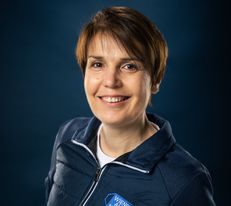 Portraitfoto Wiener Alpen Mitarbeiterin, die eine Jacke mit Wiener Alpen Logo trägt und vor einem dunklem Hintergrund steht.