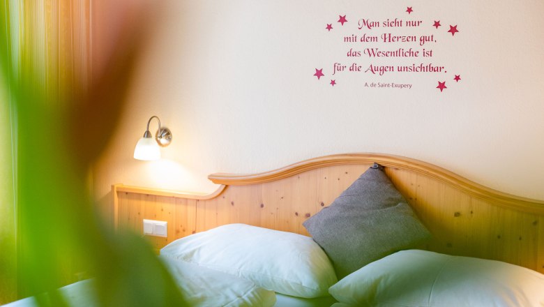 Gemütliches Schlafzimmer mit Zitat an der Wand und Holzkopfteil.