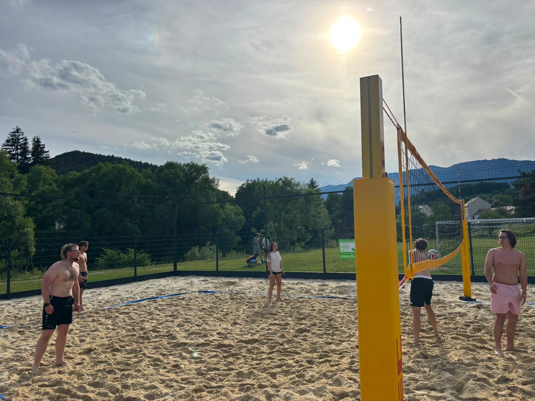 People playing beach volleyball on a sand court in sunny weather.