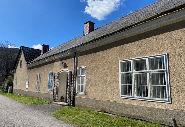 Ferienwohnung Pleesz, © Wiener Alpen Langes, einstöckiges Gebäude mit mehreren Fenstern und einem Schrägdach unter blauem Himmel.